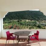 Terrasse mit Tisch und Stühlen, Blick auf grüne Hügellandschaft.