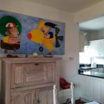 Großes Wandbild über Holzschrank, Küche mit weißen Schränken und schwarzer Arbeitsplatte.