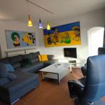 Wohnzimmer mit Sofa, Couchtisch und großen Fenstern. Wandbilder und Hängelampen sichtbar.