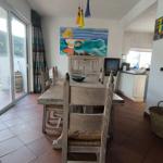 Esszimmer mit Holztisch, Stühlen und Wandbild. Küche im Hintergrund. Terrasse über Glastür.