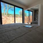 Schlafzimmer mit großem Fenster und Blick auf Steinmauer und Bäume