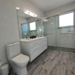 Badezimmer mit Dusche, Waschbecken und Toilette. Holzoptik Boden.