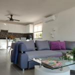 Wohnzimmer mit Sofa, Glas-Tisch und Küchenbereich im Hintergrund.