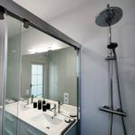 Badezimmer mit Dusche, Waschbecken und Toilette. Glaswand und Spiegel sichtbar.