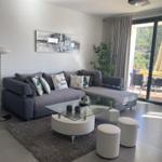 Wohnzimmer mit grauem Sofa, Glas-Tisch und Blick auf Balkon.