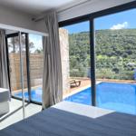 Zimmer mit Blick auf Pool und grüne Hügel. Große Fenster und moderne Einrichtung.