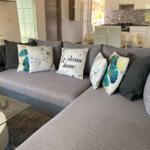 Großer grauer Sofa mit Kissen im Wohnbereich. Küche und Essbereich sind sichtbar.