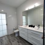 Badezimmer mit Doppelwaschbecken, Spiegel und Dusche.