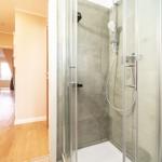 Dusche mit Glaswand und grauen Fliesen. Blick in Wohnbereich mit Holzboden.