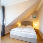 Schlafzimmer mit Dachschrägen, Bett, Nachttisch und Fenster mit Vorhang.