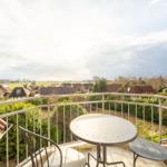 Balkon mit Tisch und Stühlen. Blick auf Dächer und Grünflächen.