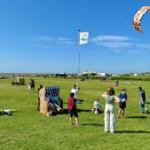 Grünes Feld am Strand mit Menschen, Strandkörben und einem Kitesurfer.