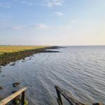 Meer und Wattlandschaft mit Steinschutz und Holzgeländer im Vordergrund.