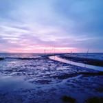 Ein Mensch steht am Ufer eines Flusses bei Sonnenuntergang mit farbigen Wolken.