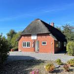 Red brick house with thatched roof and paved forecourt.