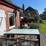 Terrace with table and chairs next to red brick house with garden.