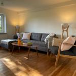 Living room with sofa, armchair, and wooden table. Window with view of trees.