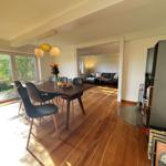 Dining area with table, chairs, and garden view. Living room in the background.