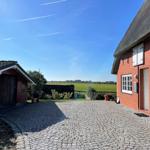 Red brick building with thatched roof and cobblestone path. Green fields in the background.