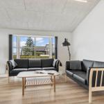 Wohnzimmer mit zwei Sofas, Couchtisch und TV. Große Fenster mit Blick auf Außenbereich.