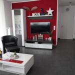 Wohnzimmer mit roter Wand, TV, Couch und Tisch.