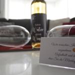 Ein Glas und eine Flasche Wein stehen auf einem Tisch. Eine Karte wünscht angenehmen Aufenthalt.