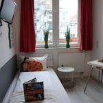 Kinderzimmer mit Bett, Hochstuhl und Fenster mit roten Vorhängen.