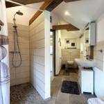 Badezimmer mit Dusche, Waschbecken und Toilette. Holzbalken an der Decke.