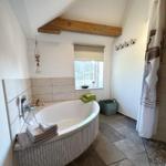 Bad mit Badewanne, Fenster und Holzbalken an der Decke.