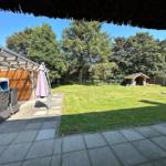 Terrasse mit Sitzgelegenheiten und Grillplatz im Garten. Hintergrund: Wald und Holzgarage.