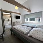 Schlafzimmer mit Doppelbett, Fenster und Blick in die Küche.