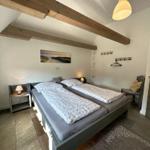 Schlafzimmer mit Doppelbett, Holzbalken, Nachttisch und Stuhl.