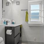 Badezimmer mit Waschbecken, Spiegel und Fenster. Grün Handtuch hängt an Wandhalter.
