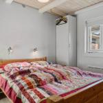 Schlafzimmer mit Holzbett, weißer Wand und Fenster. Kleiderständer und Nachttisch sichtbar.