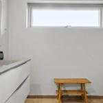 Badezimmer mit Waschbecken, Spiegel, Holzbank und Fenster.