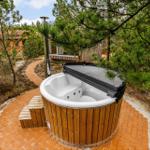 Ein Whirlpool mit Holzrahmen auf einem Kiesweg zwischen Bäumen.