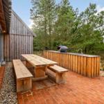 Terrasse mit Holztisch, Banken und Grill. Hintergrund: Bäume und Holzwände.