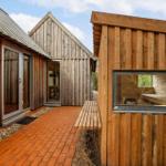 Holzgebäude mit Terrasse und Sauna. Roter Klinkerweg und Fenster zur Sauna.
