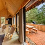 Haus mit Holzverkleidung, Küche, Essbereich und Terrasse mit Grill und Bänken.