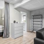 Schlafzimmer mit Bett und Vorhang. Wohnbereich mit Sofa und Regal. Küche im Hintergrund.