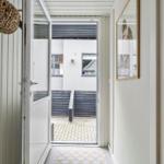 Hausgang mit offener Tür zum Hof mit Steinplatten und dunklem Holzgeländer.