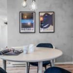 Runde Tisch mit blauen Stühlen, zwei Wandposter und Pendelleuchten.
