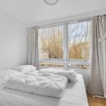 Schlafzimmer mit weißem Bett, Fenster und Gardinen.