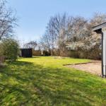 Grüner Garten mit Holzhaus und blühenden Bäumen im Hintergrund.