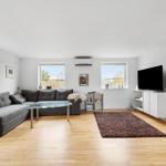 Wohnzimmer mit grauem Sofa, Glas-Tisch und braunem Teppich.