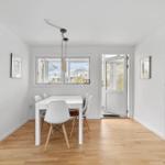 Essbereich mit weißem Tisch, Stühlen und Holzboden. Fenster und Tür führen nach draußen.