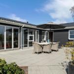 Terrasse mit Tisch, Stühlen und Sonnenschutz vor einem Haus mit Glaswänden.