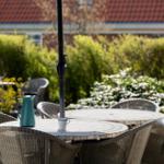 Terrasse mit Tisch, Stühlen und Kaffeetasse. Hintergrund: grüne Hecke und Haus.