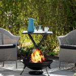Zwei Stühle und ein Tisch um einen brennenden Feuerkessel im Garten.