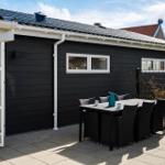Schwarzes Haus mit Terrasse und Sitzgruppe. Glastür führt ins Innere.